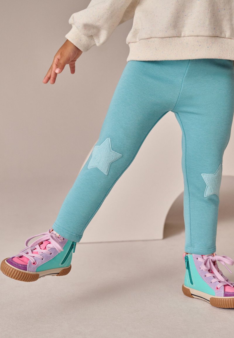 Akvablå leggings med lyseblå stjerneapplikationer på knæene, parret med flerfarvede høje sneakers med lynlåse.
