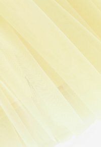 Jasnożółta siateczkowa tkanina o delikatnej, przewiewnej strukturze, fałdy tworzące efekt warstwowy, charakteryzująca się przezroczystością i subtelną półprzezroczystością.