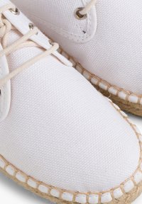 Valged kangast espadrillid ümarate varvastega, beež jute tallaga ja beeži nööbiga disainiga. Omab läikivaid hõbedasi auke.