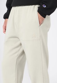 Lichtgrijze sweatpants van zachte stof, met zijzakken en een subtiel geborduurd logo op de dij. Relaxed fit en elastische tailleband.