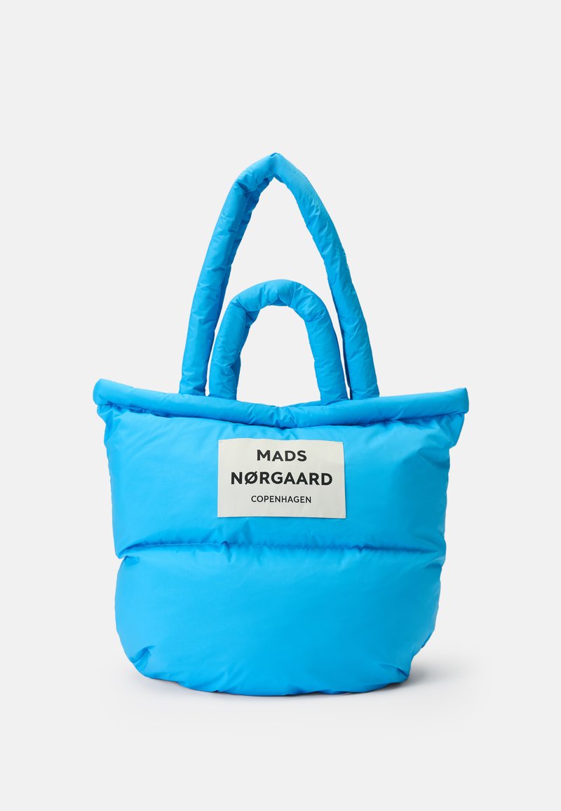 Klart blå vadderad tote-väska med två handtag och en vit etikett som står "Mads Nørgaard Copenhagen" på framsidan.