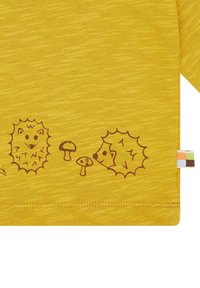 Gelbes gestricktes Shirt mit strukturiertem Finish und braunen Illustrationen von Igeln und Pilzen entlang des unteren Randes.