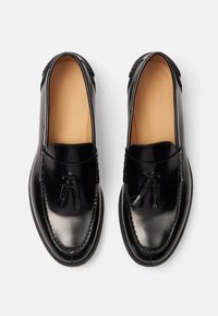 Czarne skórzane mokasyny o gładkim wykończeniu, z wykończeniami w postaci frędzli oraz dekoracyjnym przeszyciem wzdłuż brzegów. Elegancki, migdałowy kształt.