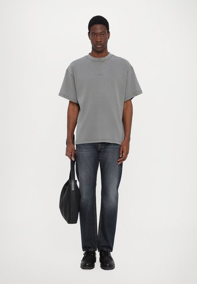 Grå överdimensionerad bomullströja med rund halsringning, tillsammans med mörka jeans i denim och svarta läderskor, hållande en svart tote-väska.