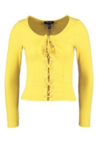 Žlutý top s dlouhým rukávem a žebrovanou texturou, který má přední šněrování a kulatý výstřih, vyrobený z elastického materiálu pro přiléhavý vzhled.