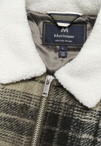 Jachetă cu carouri maro și negru, cu guler din fleece alb, fermoar argintiu și eticheta interioară albastră marcate "Matinique," mărimea L.  Material din lână texturată.