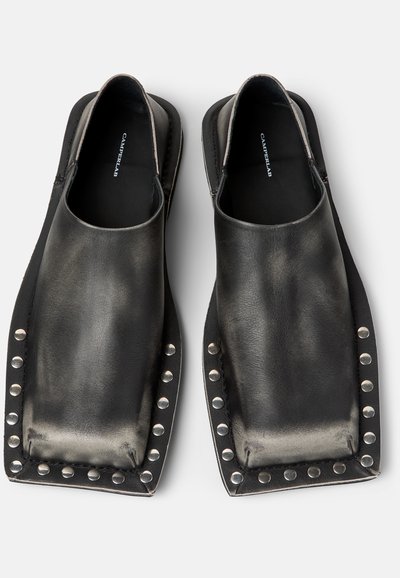 Chaussures en cuir noir faciles à enfiler, avec des bouts carrés exagérés et des clous argentés tout autour des bords, marque CamperLab à l'intérieur.