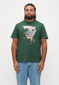 Πράσινο βαμβακερό μπλουζάκι με γραφικό ενός φτερωτού αλόγου και το κείμενο «JACK JONES» από πάνω. Κοντά �μανίκια και άνετη εφαρμογή. Φορεμένο με ανοιχτόχρωμα μπλε τζιν.