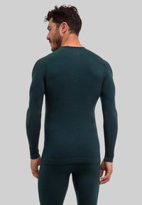 Ciemnozielona termiczna warstwa bazowa wykonana z teksturowanej tkaniny, z długimi rękawami, okrągłym dekoltem i dopasowanym krojem.