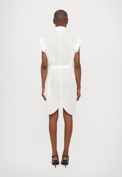 White, short-sleeved shirt dress with a high collar, belted waist, and curved hemline. Smooth fabric, minimalist design, no patterns.