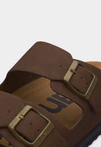 Καφέ σανδάλι με δύο ρυθμιζόμενες μπρούτζινες αγκράφες και μαλακό πέλμα, σχεδιασμένο για καθημερινή χρήση και άνεση.