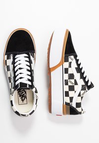 Baskets Vans à carreaux noirs et blancs avec des lacets blancs, des bouts en daim et des semelles épaisses blanches avec une semelle extérieure marron.