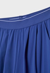 Plava suknja s naborima i elastičnim pojasom koji ima malu tkaninsku petlju i tanku bijelu liniju kao detalj.