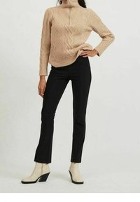 Maglione beige a trecce con collo alto, abbinato a pantaloni neri aderenti e stivaletti crema con tacco nero.