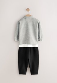 Suéter gris con capa inferior blanca, combinado con pantalones jogger negros cónicos. Tela suave, cuello redondo y detalle de botones en las mangas.