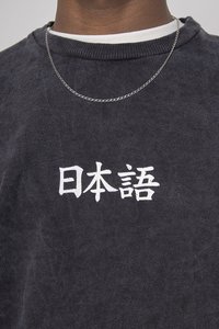 Fekete pulóver fehér japán szöveggel az elején. Bordás kerek nyakkivágás és laza szabás, vékony ezüstlánc nyaklánccal párosítva.