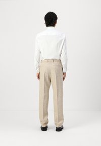 White long-sleeve shirt paired with beige textured trousers, featuring a straight-leg cut and visible back pockets. Solid black shoes.