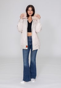 Hellbeige Bomberjacke mit einem Kragen aus Kunstfell, Reißverschluss vorne und gerippten Bündchen, kombiniert mit weit geschnittenen blauen Jeans und weißen Sneakers.