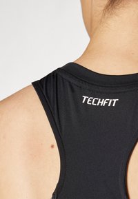Débardeur de sport noir sans manches avec une texture lisse, portant le nom de la marque "TECHFIT" imprimé en blanc au dos.