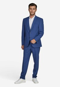 Blauer Anzug mit feinem Muster, einreihige Jacke, mit Schößchen und passender Hose, kombiniert mit einem weißen Hemd und weißen Sneakern.