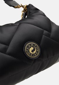 Czarna pikowana torebka wykonana z gładkiego materiału, z złotą, okrągłą naszywką z logo i złotym łańcuszkiem ozdobnym. Zamknięcie na zamek błyskawiczny na górze.