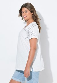 Camiseta blanca de manga corta, con un diseño de estrella de mar y costura decorativa. Combinada con pantalones cortos de mezclilla azul claro.