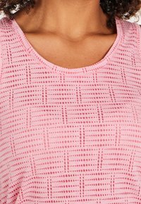 Close-up of a person wearing a pink sleeveless top with a patterned grid of dotted lines and short horizontal stripes.