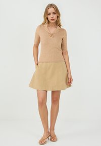 Haut beige à manches courtes côtelé avec un col et un bouton doré, associé à une jupe évasée beige avec des poches latérales. Texture lisse.