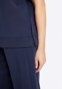 Marineblauw top met korte mouwen, voorzien van een zijsplit en een gladde textuur, gecombineerd met bijpassende wijde broek.