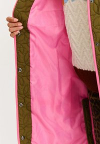 Prešívaná bunda so zeleným vonkajším materiálom a kontrastnou ružovou vnútornou podšívkou. Má patentky, textúru s listovým vzorom a žiarivé farby.