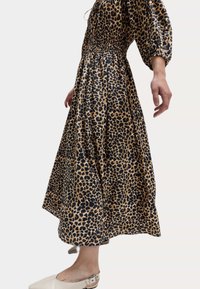 Šaty s leopardím potiskem v béžové a černé barvě, mají smockovaný živůtek, balónové rukávy a splývavou sukni. Nosené s světlými botami.