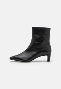 Botine negre din piele, cu vârf ascuțit și toc coborât, curbat. Textură netedă și design minimalist. Fără modele sau accente vizibile.