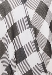 Tissu à vichy noir et blanc avec des carrés unis et rayés alternés, présentant un détail de couture en gros plan.