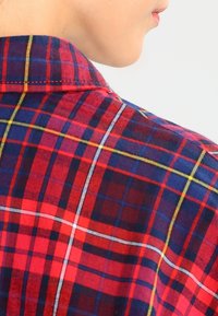 Collo a camicia a scacchi rossi e blu con accenti gialli e bianchi, caratterizzato da un tessuto testurizzato e dettagli di cucitura visibili.