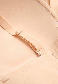 Interno di un reggiseno beige con tessuto morbido e liscio. Presenta spalline regolabili, chiusura a gancetto e cuciture piatte per il massimo comfort.