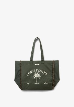 Sac cabas vert foncé avec le texte "SUNSET LOVER the beach club" et un motif de palmier, doté de deux anses et de coutures latérales à franges.