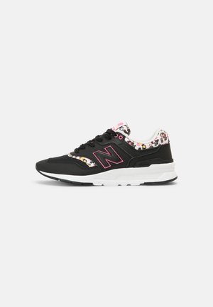 Baskets New Balance noir et blanc avec des accents roses et des détails d'imprimé léopard multicolore sur le col et la languette, logo latéral visible.