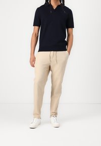Granatowa koszulka polo z krótkim rękawem i dekoltem w serek, o gładkiej fakturze, w połączeniu z jasnobeżowymi, luźnymi lnianymi spodniami oraz białymi trampkami.