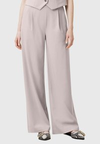 Pantaloni larghi grigi chiari realizzati in tessuto morbido con pieghe frontali, abbinati a scarpe bianche e nere con motivo e una fibbia decorativa.