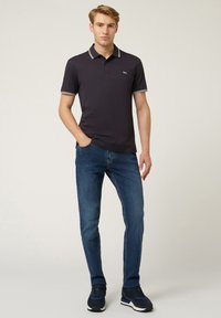 Polo shirt navy con accenti bianchi, maniche corte e un logo discreto. Abbinato a jeans blu e sneakers scure, che mostrano un look informale.