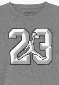 Graues T-Shirt mit einer großen, strukturierten "23" Grafik in Schwarz und Weiß, die die Silhouette eines Spielers in einer Sprungpose zeigt.