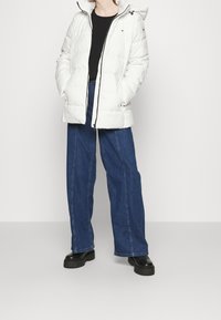 Vit puffjacka med huva, med dragkedjestängning och framfickor, i kombination med lösa blå denimbyxor och svarta platåstövlar.