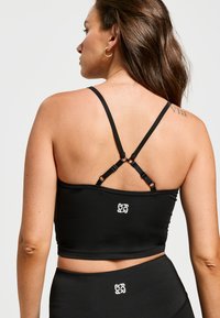 Zwarte sport crop top met verstelbare kruisbanden, gemaakt van een zachte stof. Heeft een klein logo op de rug en een aansluitend ontwerp.