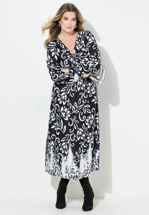 Schwarz-weißer Blumenprint-Kleid mit langen Ärmeln, tiefem V-Ausschnitt und einem fließenden Rock; kombiniert mit schwarzen Stiefeletten und einem silbernen Clutch.