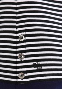 Chemise à rayures noires et blanches avec quatre boutons, présentant une texture côtelée et un petit logo brodé dans le coin inférieur droit.