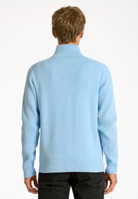 Ljust blå ribbad stickad tröja med hög krage, långa ärmar och rak fåll. Texturerat material med avslappnad passform.