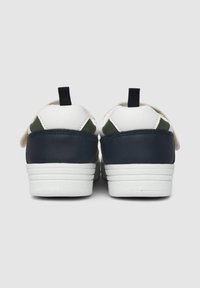 Sneakers bianchi e navy con accenti verdi, caratterizzati da una finitura in pelle liscia, un tallone testurizzato e una linguetta sul retro.