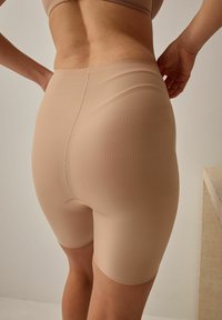 Huidkleurige compressie shorts met een gladde textuur, midden boven de dijen, en een klein uitsnede detail aan de achterkant. Naadloos ontwerp.