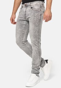 Jeans skinny de mezclilla gris con un acabado desgastado, que cuentan con un clásico diseño de cinco bolsillos y costuras en contraste, combinados con zapatillas blancas.