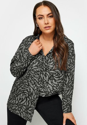 Button-up shirt in dark gray fabric featuring a black leaf pattern. The design has a relaxed fit with long sleeves and a V-neckline.